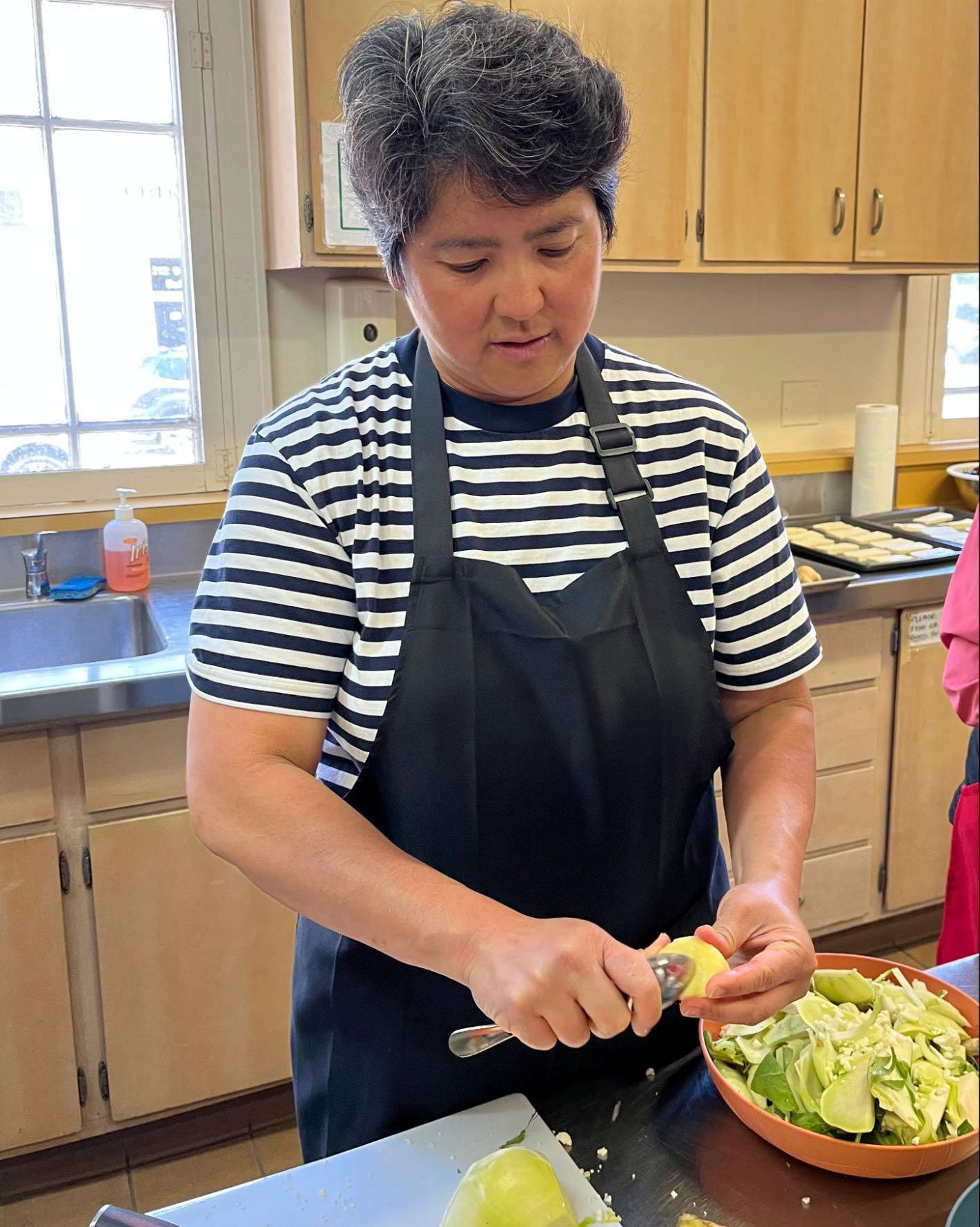 A person chopping vegetables into a bowl in a commercial kithen.