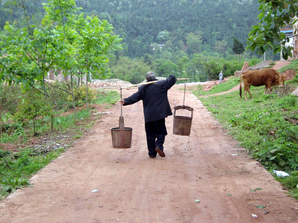 A person carrying farm implements on a rural road