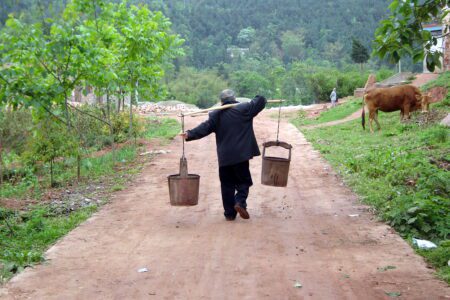 A person carrying farm implements on a rural road