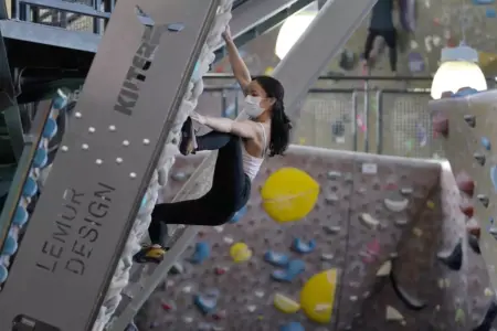 A woman claiming a rock wall in a gym while wearing a face mask